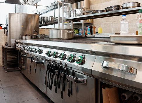 A chef is preparing food in the restaurant's kitchen. Selective focus on a pan on the stove.