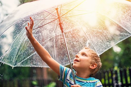 Little boy enjoying spring or summer rain. The boy aged 6 is holding the umbrella and checking the rain with smile.