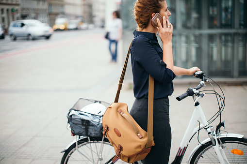 Young woman using her mobile phone while riding the bicycle around the city 