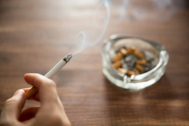 燃えるタバコを手に持つ若い女性 - 喫煙問題 ストックフォトと画像