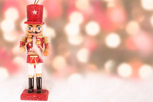 Close-up view of an elegant red Christmas nutcracker ornament on snow white background with colorful holiday lights.  Copyspace at side.  NOTE:  This image created for the Getty Creative Content Brief #663372617.   This ornament is not original artwork.