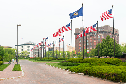 Omaha, United States - May 7, 2016: American flags line the landscaped street, ConAgra Drive which leads to the ConAgra Foods business. People walk in the distance with a stroller. Historic buildings fill the background.