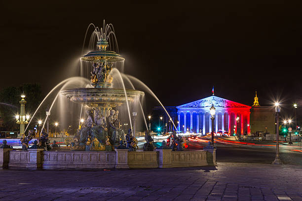 Paris, France - July 28, 2016: Fontaine des Mers at night. Palais Bourbon with the French Flag illuminated on it can be seen in the distance.