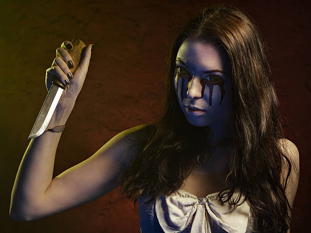 Vampire girl with a knife. Blood leaks from her eyes stock photo