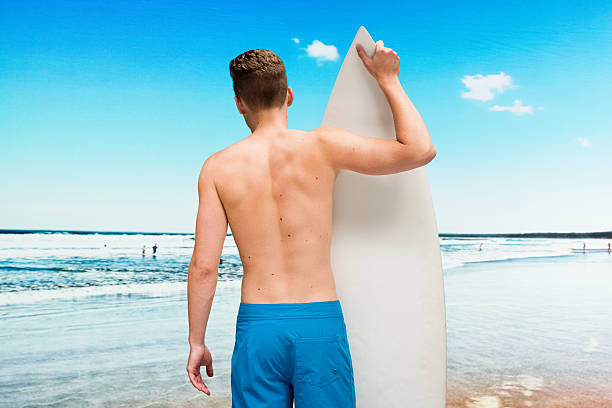 vista posteriore di un surfista in piedi alla spiaggia - sport chest men adolescence foto e immagini stock