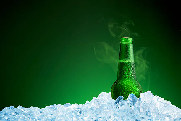Bottle of cold beer in ice on green background