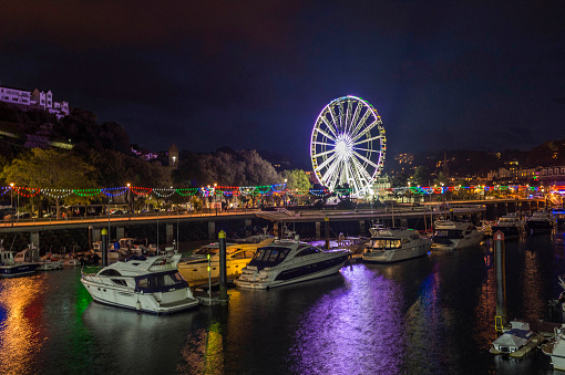 Torquay, United Kingdom - October 22, 2016: Landscape, depicting Torquay Marina and Millenium Wheel. The last of the evening light has faded and the marina, pier and wheels neon lighting becomes more prominent, illuminating the shore as the natural light diminishes. Motion blur has been introduced to capture and emphasise the rotation of the Torquay Wheel. Photograph was taken from the Princess Pier area.