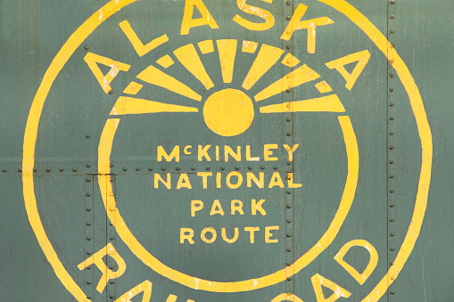 Homer, Alaska, USA - May 22, 2016: Weathered old Alaska Railroad sign for the McKinley National Park Route, painted yellow on green background, riveted steel with bits of rust.