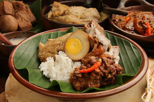 Gudeg Rice In Jogja Nasi Gudeg or Rice Dish with Gudeg is Jogjakarta's signature dish. It consists of steamed rice with Gudeg (jack fruit stew drizzled with thick coconut cream) with Opor Ayam (chicken in white curry) and Sambal Goreng Krecek (spicy stew of cattle skin crackers and red bean). The Nasi Gudeg is plated on an earthenware plate that lined with banana leaf. The plate is set on a wooden block; surrounded by the dishes that make up the complete meal. gudeg stock pictures, royalty-free photos & images