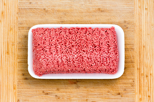 Close up on a container of fresh ground beef in retail packaging opened on a wooden cutting board ready to be prepared for a meal