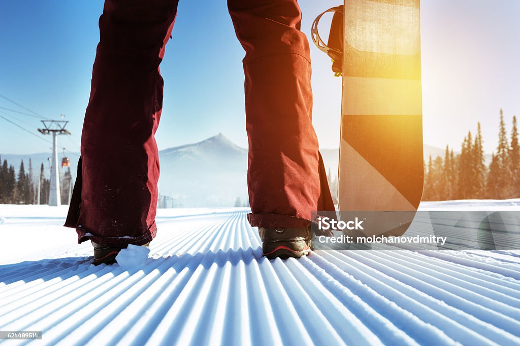 Snowboarder stands on slope backdrop Snowboarder stands on slope backdrop. Closeup legs and snowboard Skiing Stock Photo