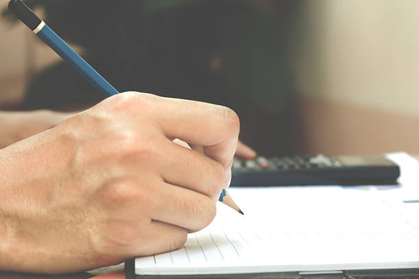 istock Man hand is writing in a notebook and calculator counting 624492108