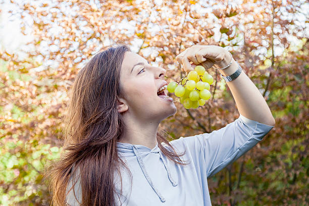 istock young beautiful girl sitting under a tree eating grapes 624495386