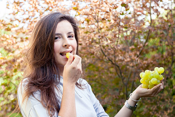 istock young beautiful girl sitting under a tree eating grapes 624495656
