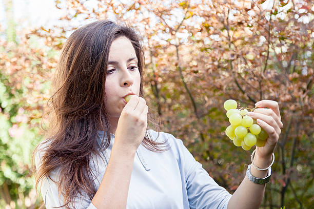 istock young beautiful girl sitting under a tree eating grapes 624496082