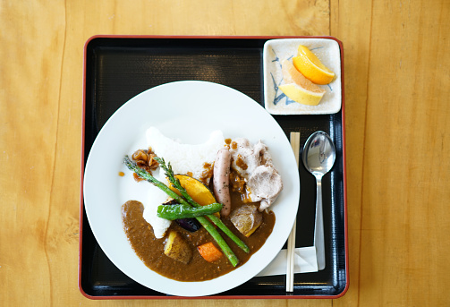 Top view of curry rice with sausage, potatoes, pumpkin, rice, artichoke, pork, fennel, curry sauce on plate. It is delicatessen, oishi, very tasty and is offered on Hokkaido, Japan. 