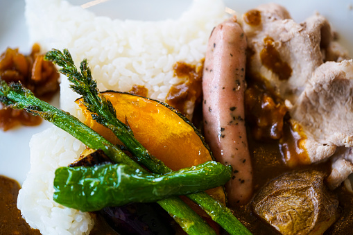 ]Top view of curry rice with sausage, potatoes, pumpkin, rice, artichoke, pork, fennel, curry sauce on plate. It is delicatessen, oishi, very tasty and is offered on Hokkaido, Japan. 