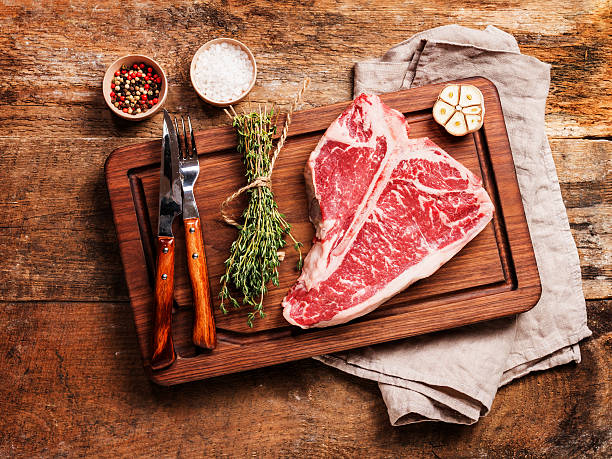 Raw T-bone Steak Raw T-bone Steak for grill or BBQ on cutting board over aged wooden background, top view porterhouse steak stock pictures, royalty-free photos & images