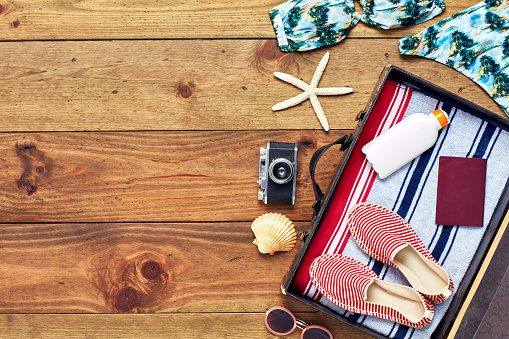 Directly above shot of open suitcase with summer vacation equipment .Flat lay of travel and beach accessories. The travel essentials are placed on right side of hardwood floor.