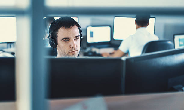 Software developers. Closeup front view of a software developers sitting in front of dual display copmputer. He has headphones on and is focused on his work. Two of his colleagues are working in background. headphones plugged in photos stock pictures, royalty-free photos & images