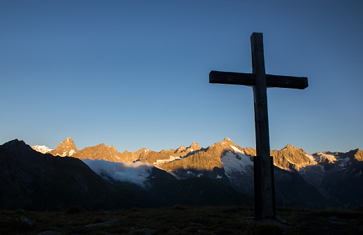 A cross silhouetted by a stunning sunrise in the alps, with Mont Blanc and Grand Jorasses in the background.