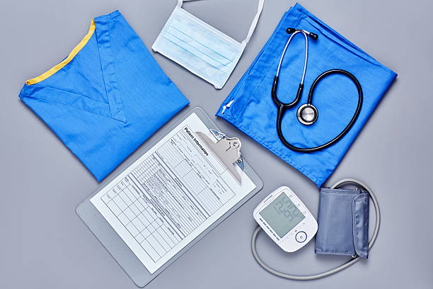 Flat lay of medical supplies on gray background Directly above flat lay shot of medical supplies. Scrubs are placed with application form blood pressure gauge stethoscope and surgical mask. All are on gray background. medical record photos stock pictures, royalty-free photos & images