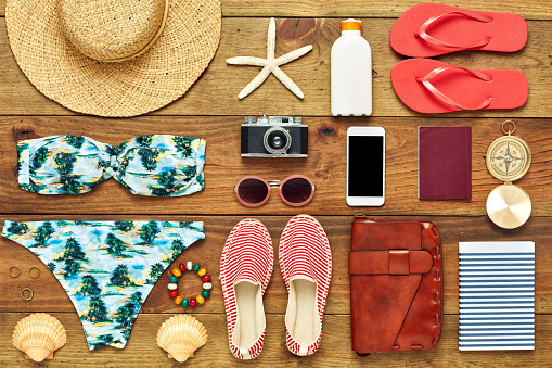 Full frame shot of summer vacation accessories. Directly above shot of travel and beach equipment flat lay. They are arranged on wooden floor.