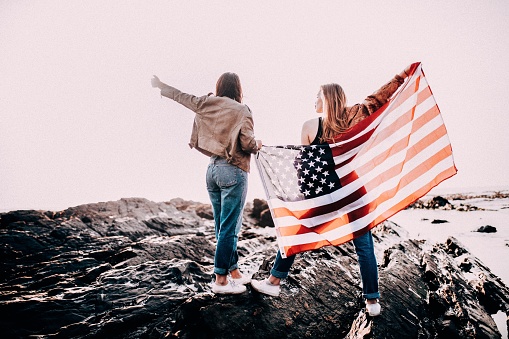 Young adult women cheering with USA flag on beach