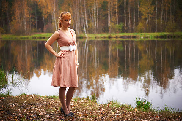 Beautiful girl in dress in autumn forest. Behind lake.