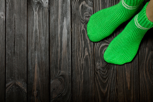 Legs knit green wool socks on wooden dark background.