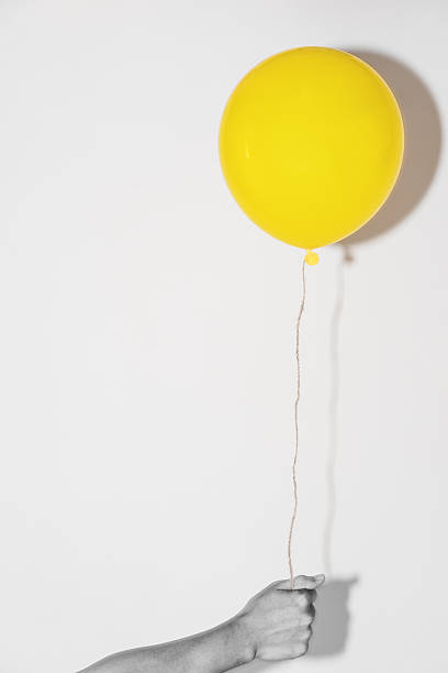 Hand holding yellow balloon on white wall with shadow reflection