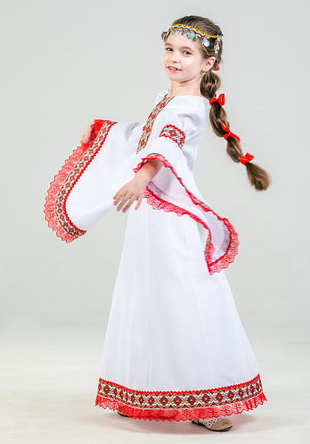 Beautiful elementary age girl with a long braid. The girl is dressed in Mari native dress and headdress made of beads and coins on her head. She is spinning in a dance. The little girl is smiling looking at the camera. Studio shooting on a white background