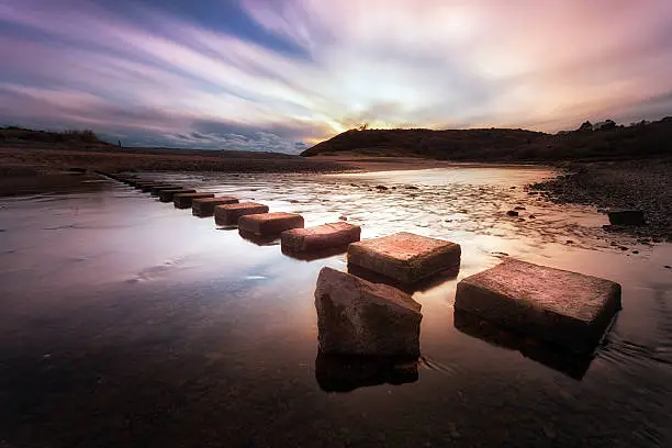 Sunset at the stepping stones that allow access to the divided beaches at Three Cliffs Bay on the Gower peninsula in Swansea, South Wales