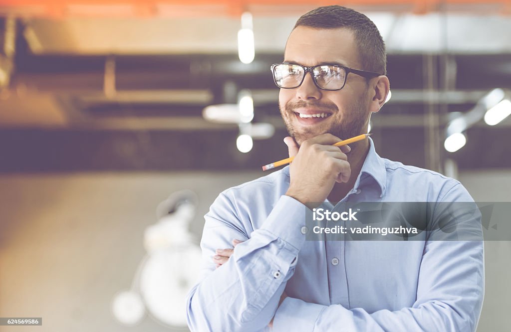 Handsome businessman working Handsome businessman in classic shirt and eyeglasses is holding a pencil, looking away and smiling while working in office Contemplation Stock Photo