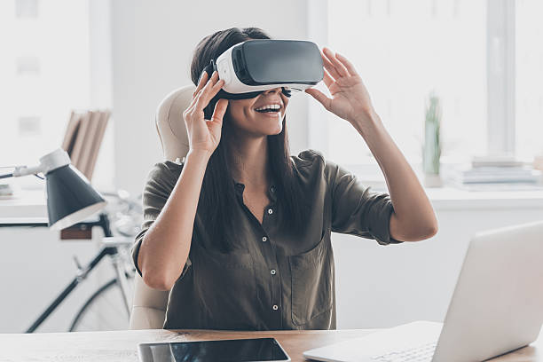 Future is right now. Confident young woman adjusting her virtual reality headset and smiling while sitting at her working place in office virtual reality stock pictures, royalty-free photos & images