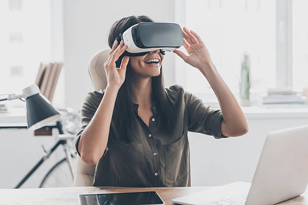 Future is right now. Confident young woman adjusting her virtual reality headset and smiling while sitting at her working place in office simulator stock pictures, royalty-free photos & images