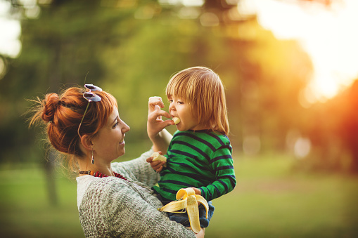 Young mother feeding bananas to her son in the park,side view