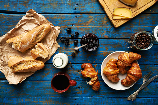 Fresh baked croissants and baguette, blackberry jam, coffee and cheese on old wooden table