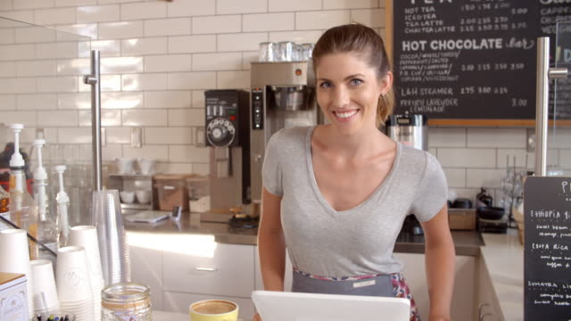 Woman behind the counter of a coffee shop crosses arms