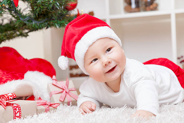 istock Baby in Santa hat next to Christmas tree with presents 624652076