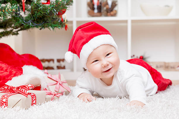istock Baby in Santa hat next to Christmas tree with presents 624652274