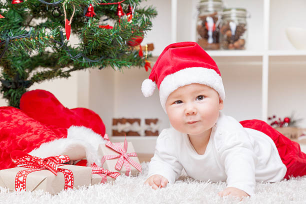 istock Baby in Santa hat next to Christmas tree with presents 624652498