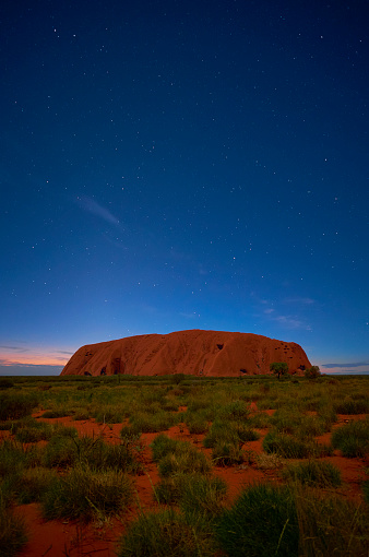 Northern Territory, Australia - March 29, 2016: Pre-dawn in the heart of the Australian Outback, and countless stars overhead gently illuminates the massive form of Uluru that looms majestically on the horizon.