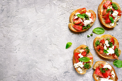 Italian bruschetta with tomatoes,feta and basil pesto on a grey concrete or stone background.Top view.