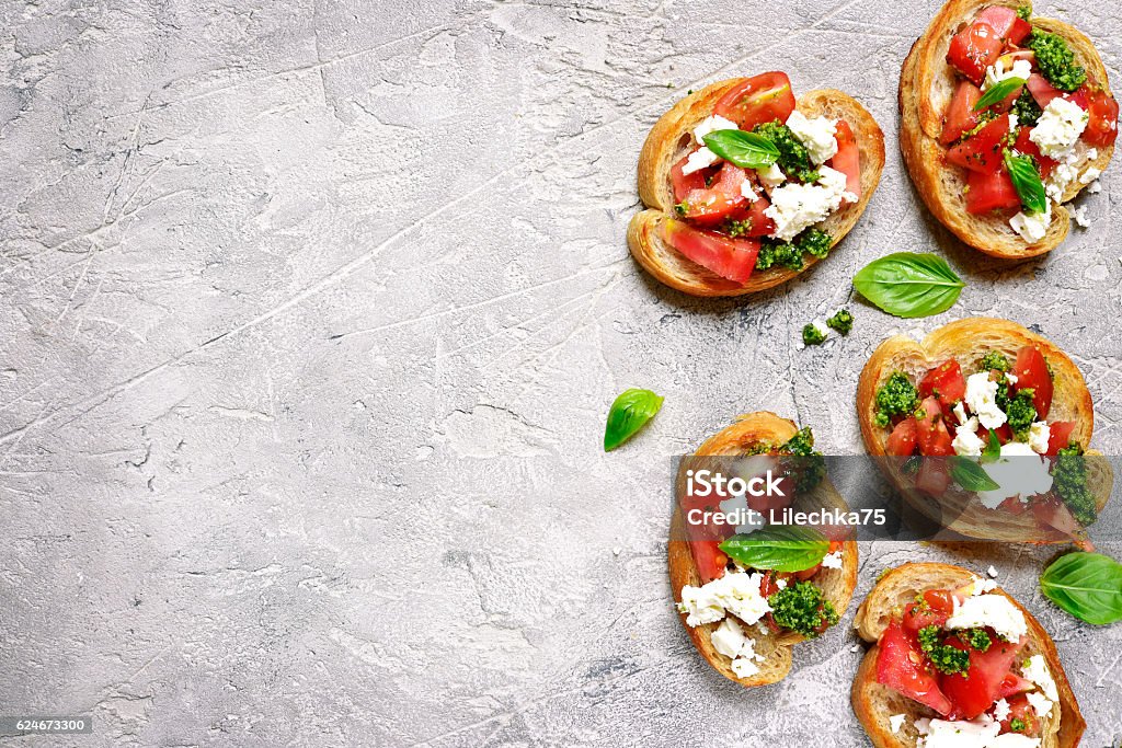 Italian bruschetta with tomatoes,feta and basil pesto on . Italian bruschetta with tomatoes,feta and basil pesto on a grey concrete or stone background.Top view. Bruschetta Stock Photo