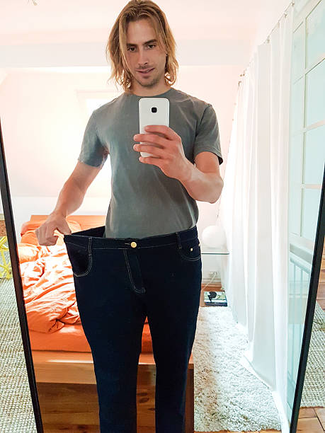 istock Young man taking selfie in mirror showing weight loss 624676670