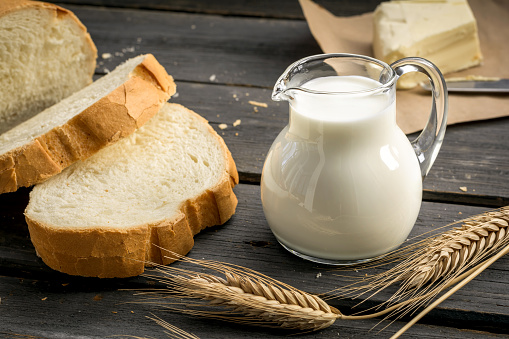 Jug of milk with sliced white bread and wheat ears on wooden background
