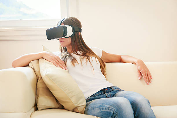 istock Young woman sitting on couch, using VR glasses 624680508