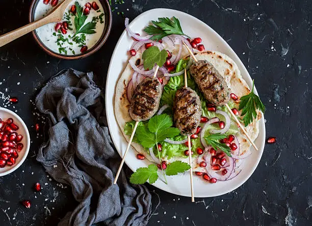 Lamb kebab on flatbread with lettuce, onions and pomegranate. On a dark background, top view