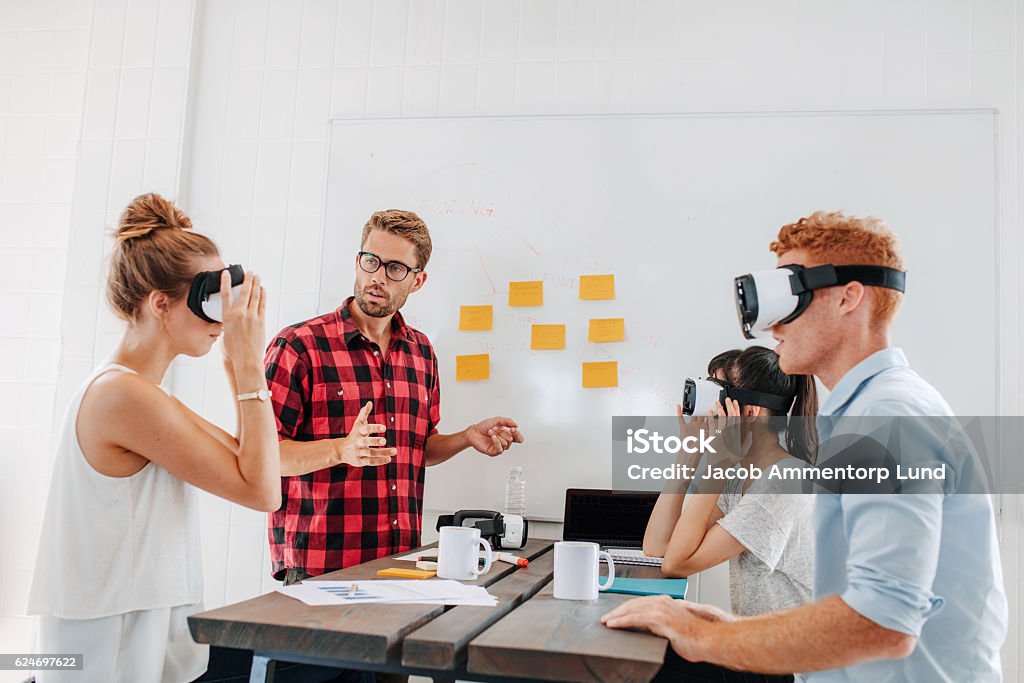 Business team testing virtual reality headset in meeting Young men and women sitting at a table with virtual reality goggles. Business team testing virtual reality headset in office meeting. Virtual Reality Simulator Stock Photo